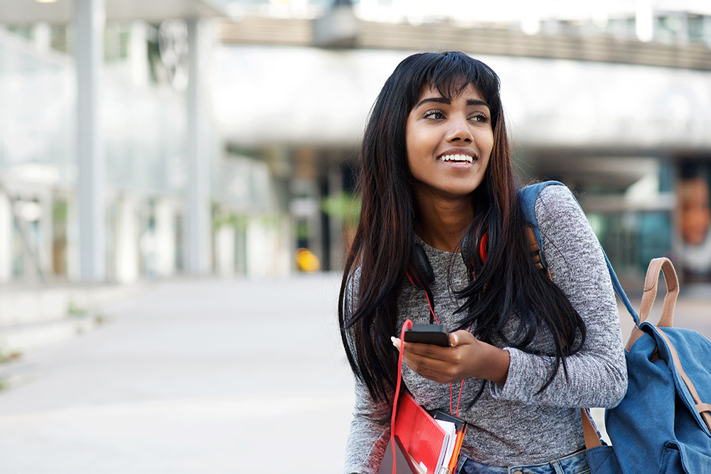 Portrait of happy Indian university student walking with mobile phone